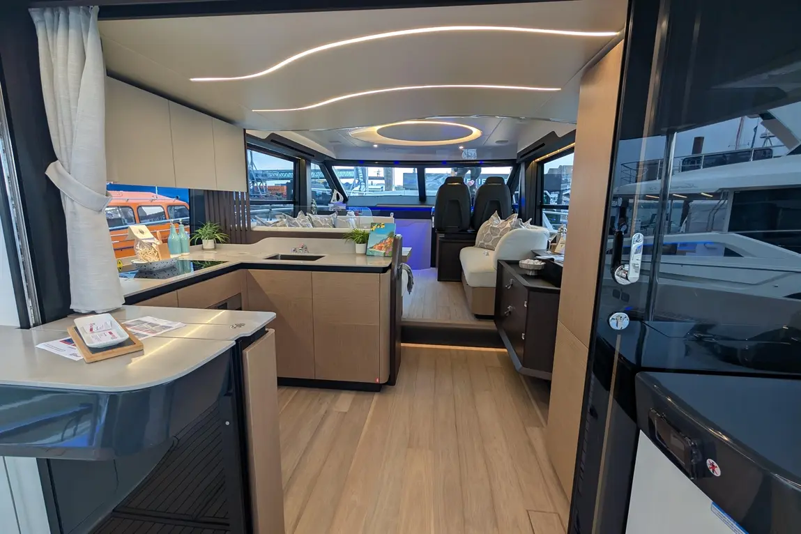 Modern yacht interior featuring a sleek kitchen, lounge area, and stylish lighting, with plush seating and marine views.